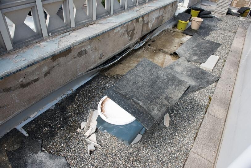 Balcony area with damaged waterproofing, loose floor coverings, and construction debris.