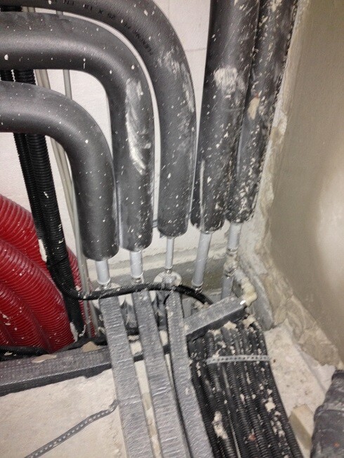 Technical room with insulated heating pipes, cables, and dust in construction condition