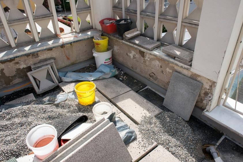 Balcony construction site with building materials, buckets, and tile slabs