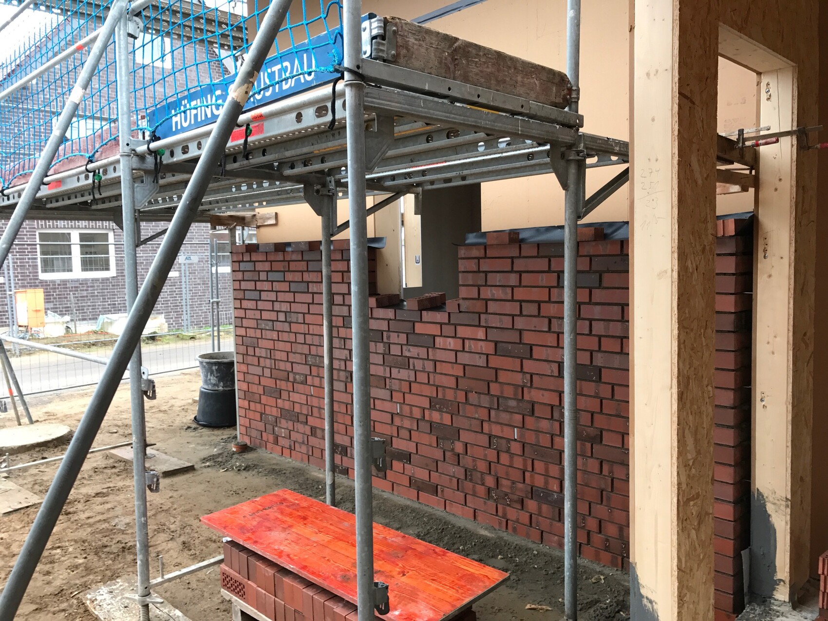 Construction site with scaffolding, red brick wall, and timber frame at shell stage