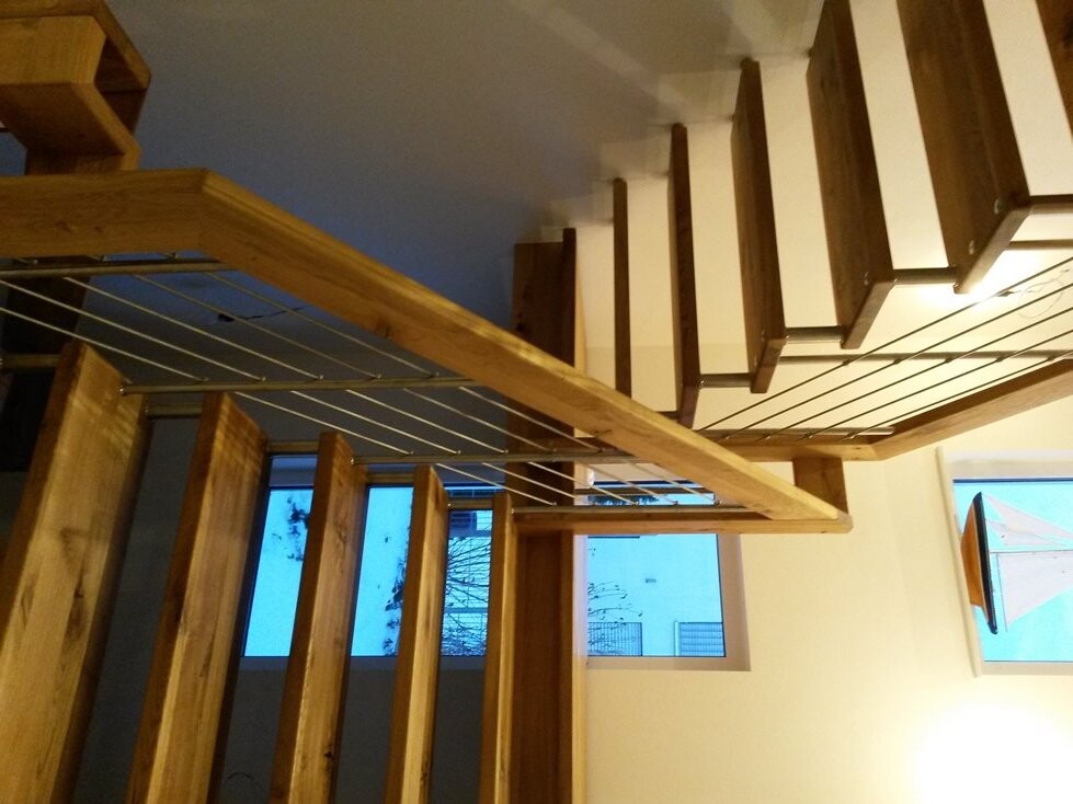 Modern wooden staircase with metal cable railing inside, window visible.