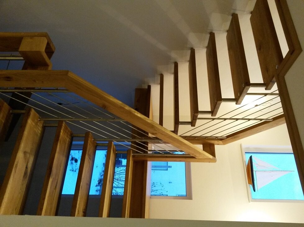 Modern wooden staircase with open risers, wire cable railing, and wooden posts inside.