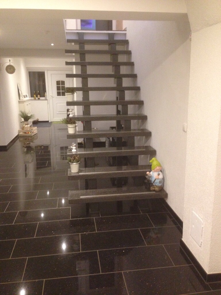Modern floating staircase with dark steps in a bright hallway, glossy floor tiles.