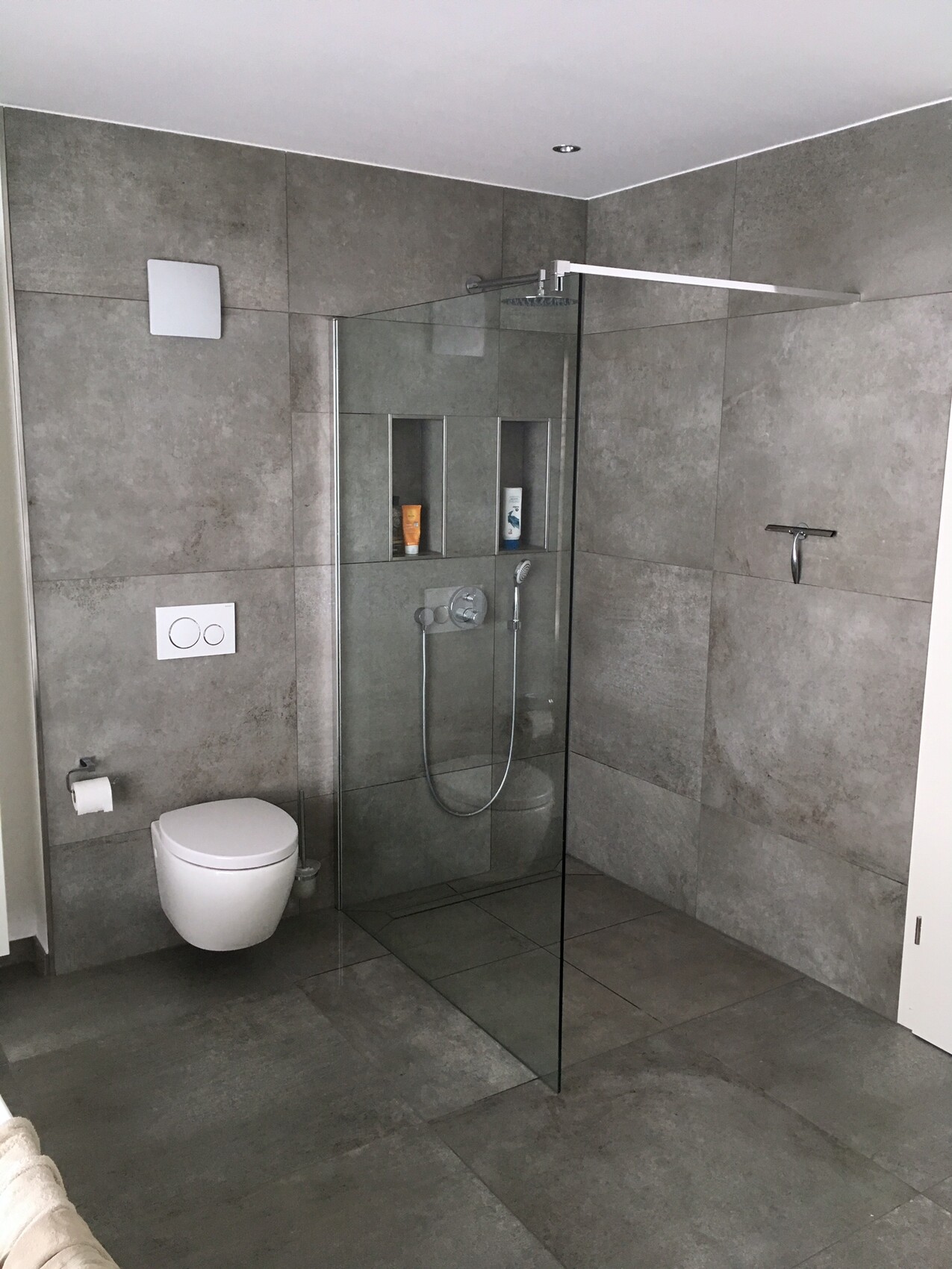 Modern bathroom with gray tiles, glass shower, wall-hung toilet, and niches with shower products.