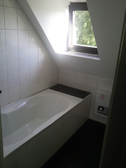 Bathroom with white bathtub, tiled walls, skylight and dark floor.