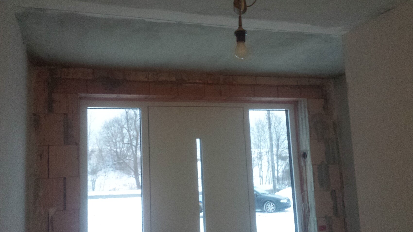 Unfinished interior with exposed brick wall, door frame, and hanging lightbulb