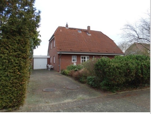 Front view of a red brick house with garage, driveway, and garden.