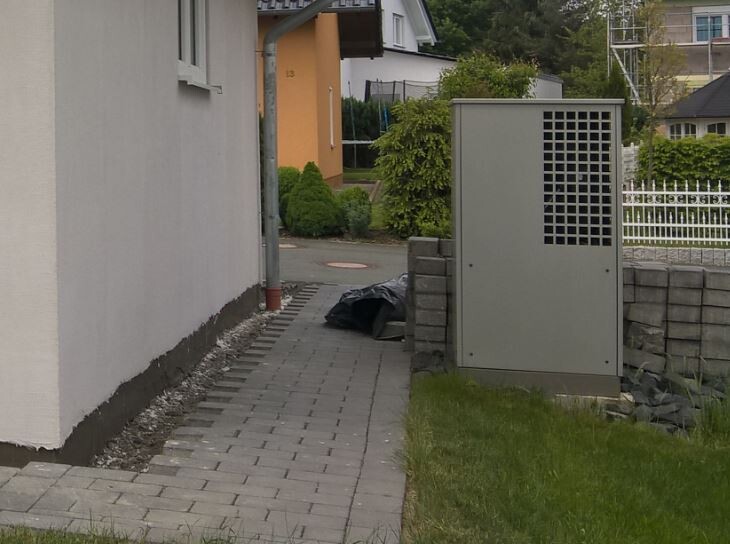Sidewalk next to residential building; to the right a gray distribution box, in front of it a black garbage bag.