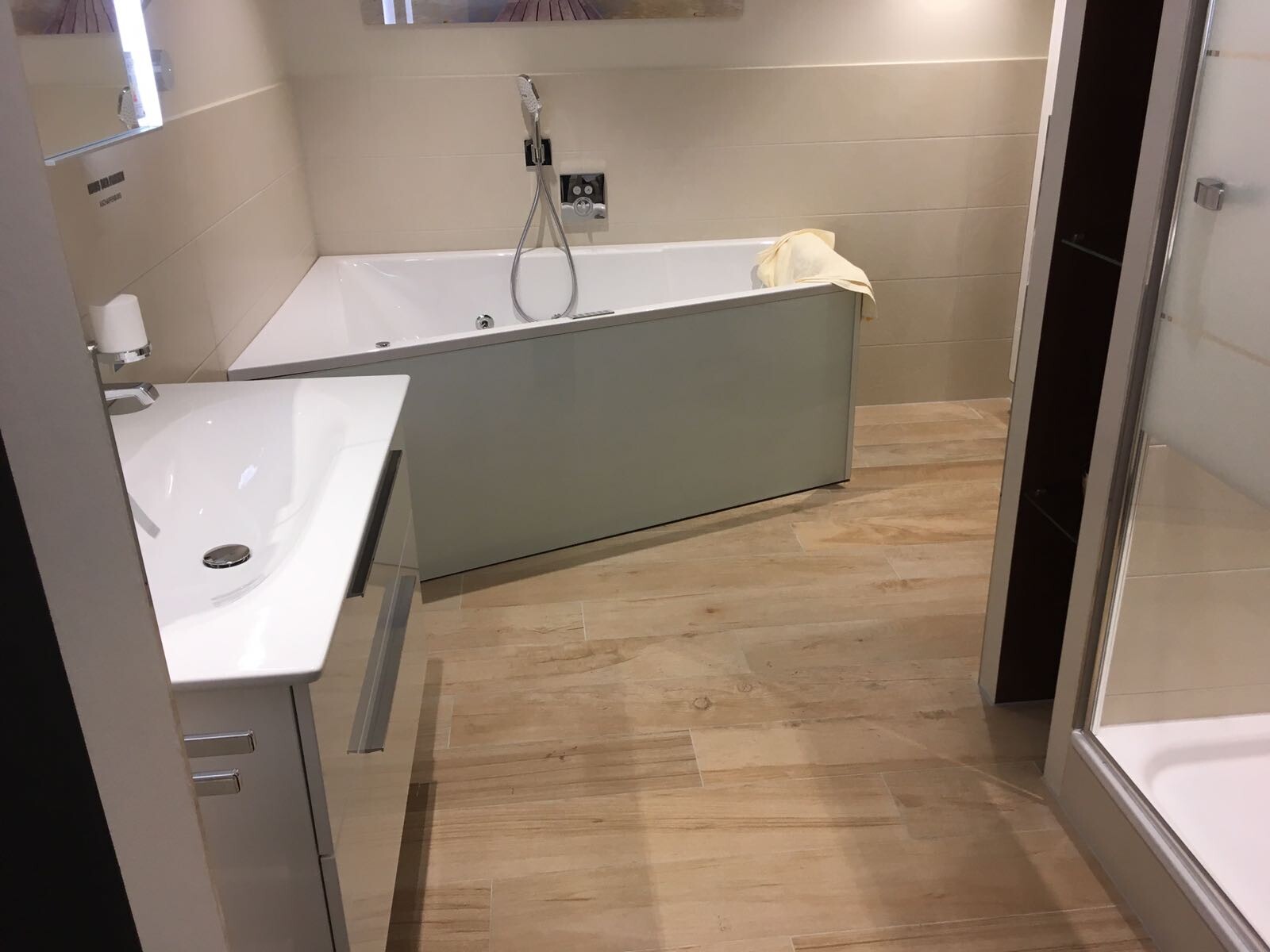 Modern bathroom with bathtub, sink, shower and wood-look floor; yellow towel over the bathtub.
