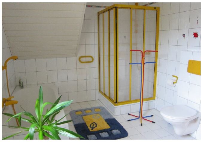 Helles Badezimmer mit gelb gerahmter Duschkabine, Toilette und Pflanze.