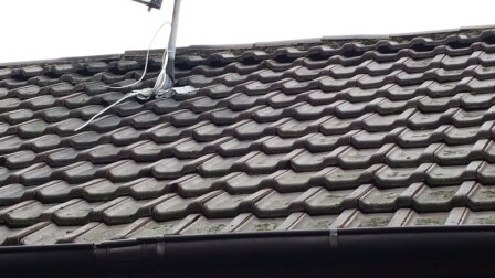 Roof with dark brown roof tiles and satellite dish on the ridge