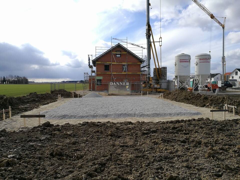Rohbau eines Hauses mit Gerüsten, Kran und Betonmischern auf einer Baustelle