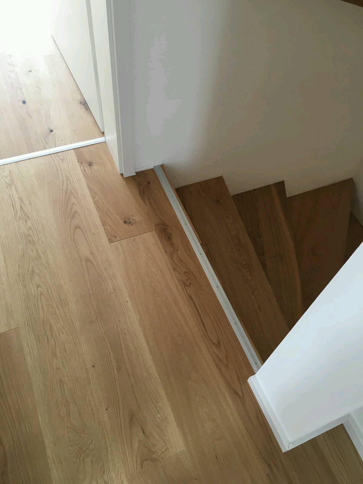 Top view of light wooden stairs, with a white wall and door frame on the side.