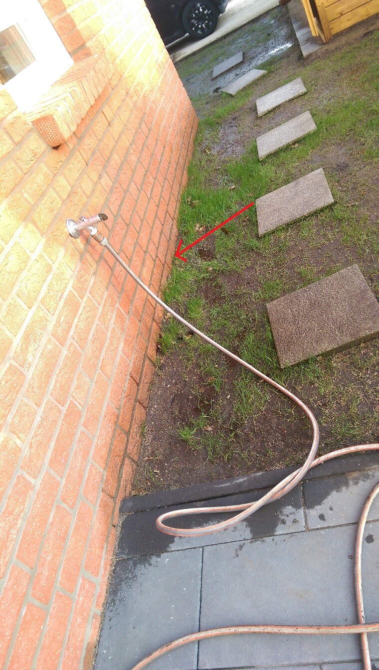 Exterior area of a house with stone slab path, grassy areas and hose on the wall