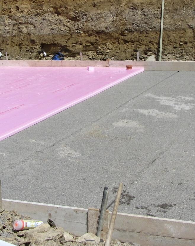 Construction site with pink insulation panels on foundation slab and visible earthworks
