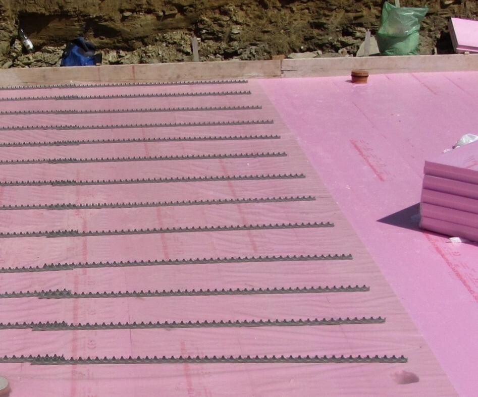 Pink insulation panels on a roof construction site with rows of insulation strips