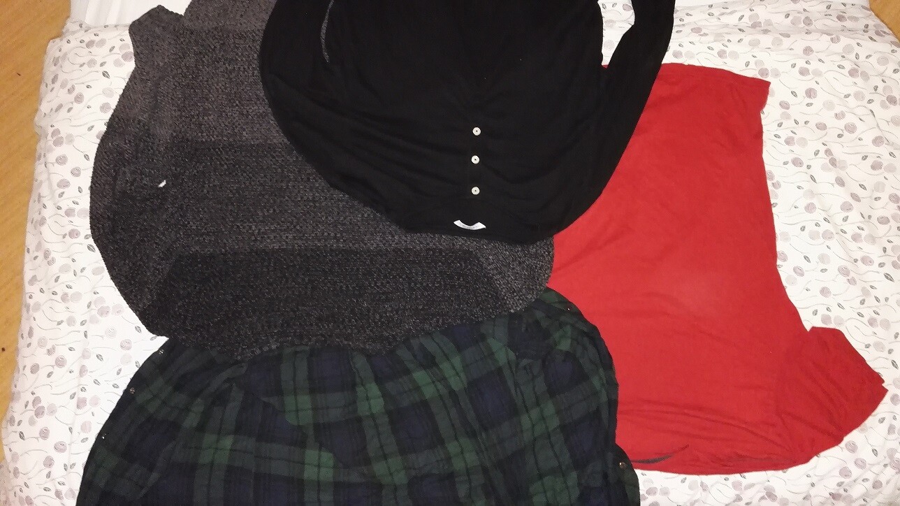 Clothing items lying on the bed: black top, gray jacket, red fabric skirt