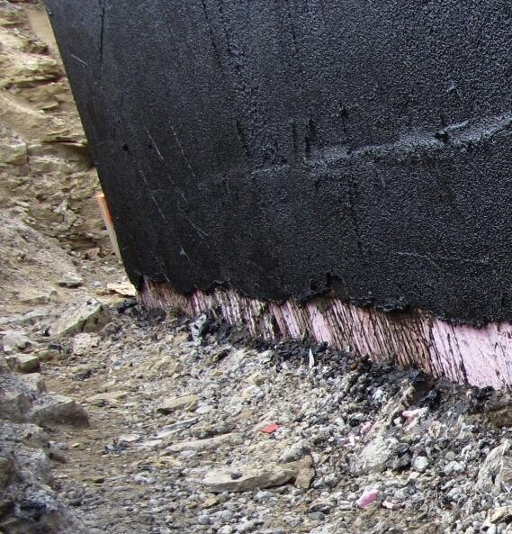 Foundation base with black waterproofing sheet and visible insulation at a construction site