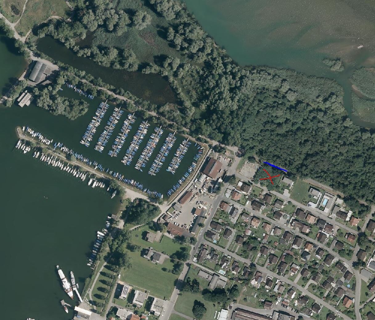 Aerial photo of a harbor with a marina full of boats next to residential buildings and green areas