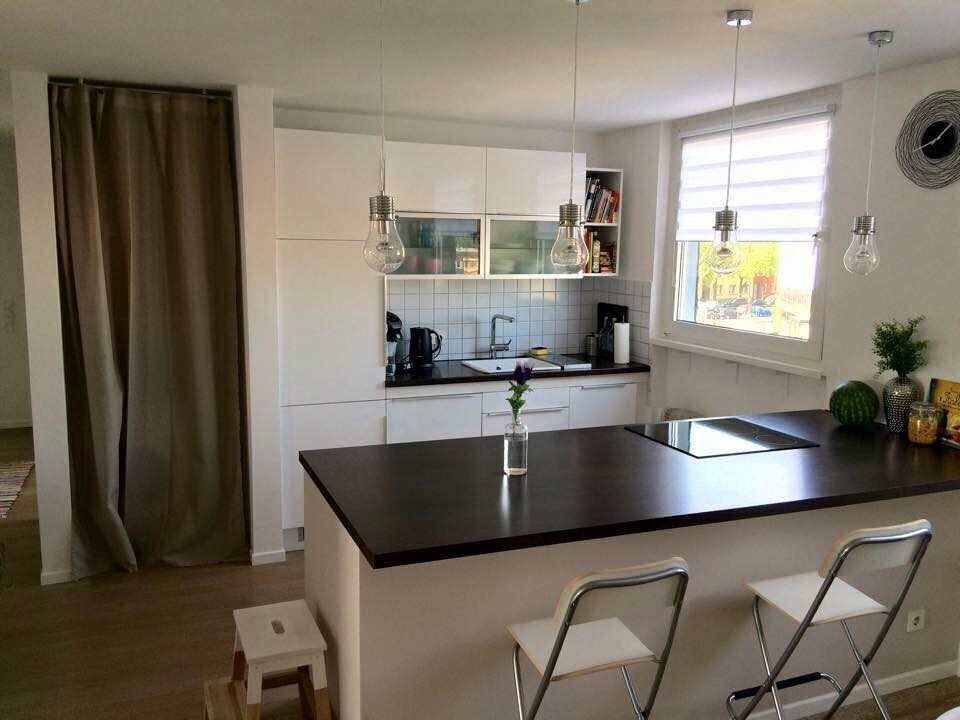 Modern kitchen with dark island, white cabinets, pendant lights, sink by the window, vase with flower.
