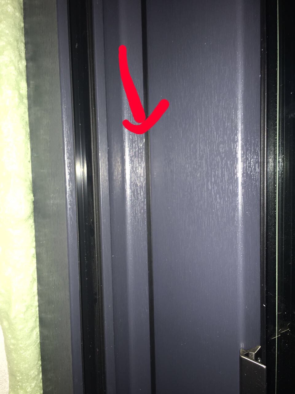 Close-up of a dark door frame with green insulation on the left, red arrow marking a gap