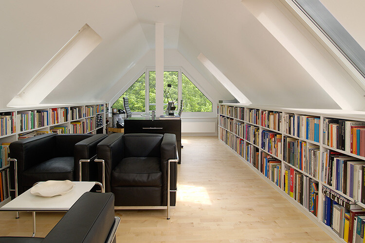 Dachgeschoss-Leseraum mit Bücherregalen links und rechts, schwarze Ledersessel, Tisch im Vordergrund