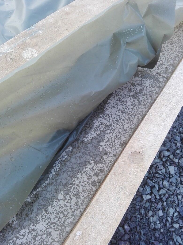 Baustelle mit grauer Schutzfolie über Holzbohlen und Fundamentplatten auf kiesigem Untergrund