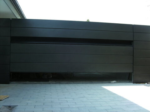 Modern dark garage door in front of a driveway paved with concrete slabs.