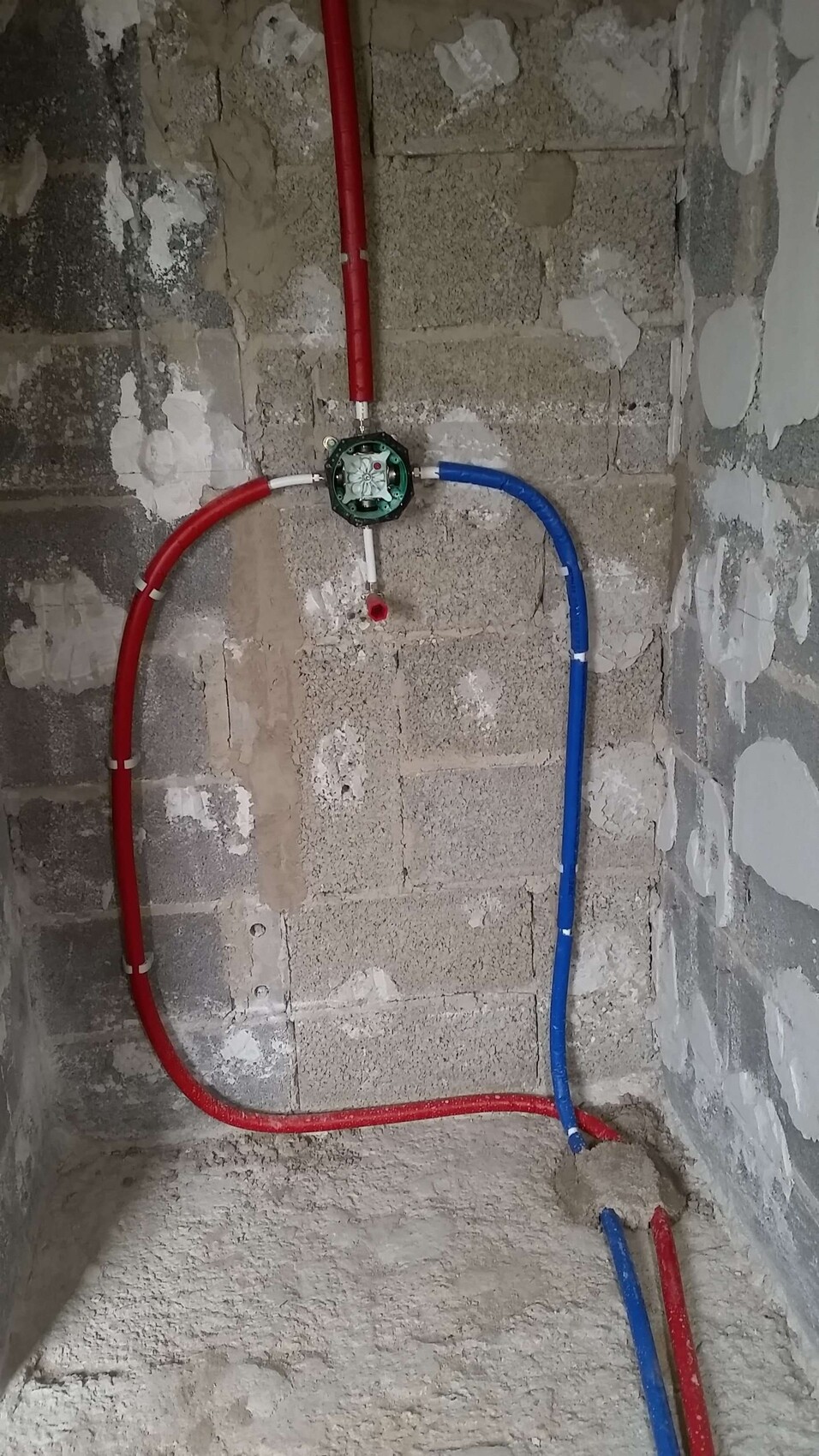 Red and blue water lines leading to a green round valve body on a shell construction site.