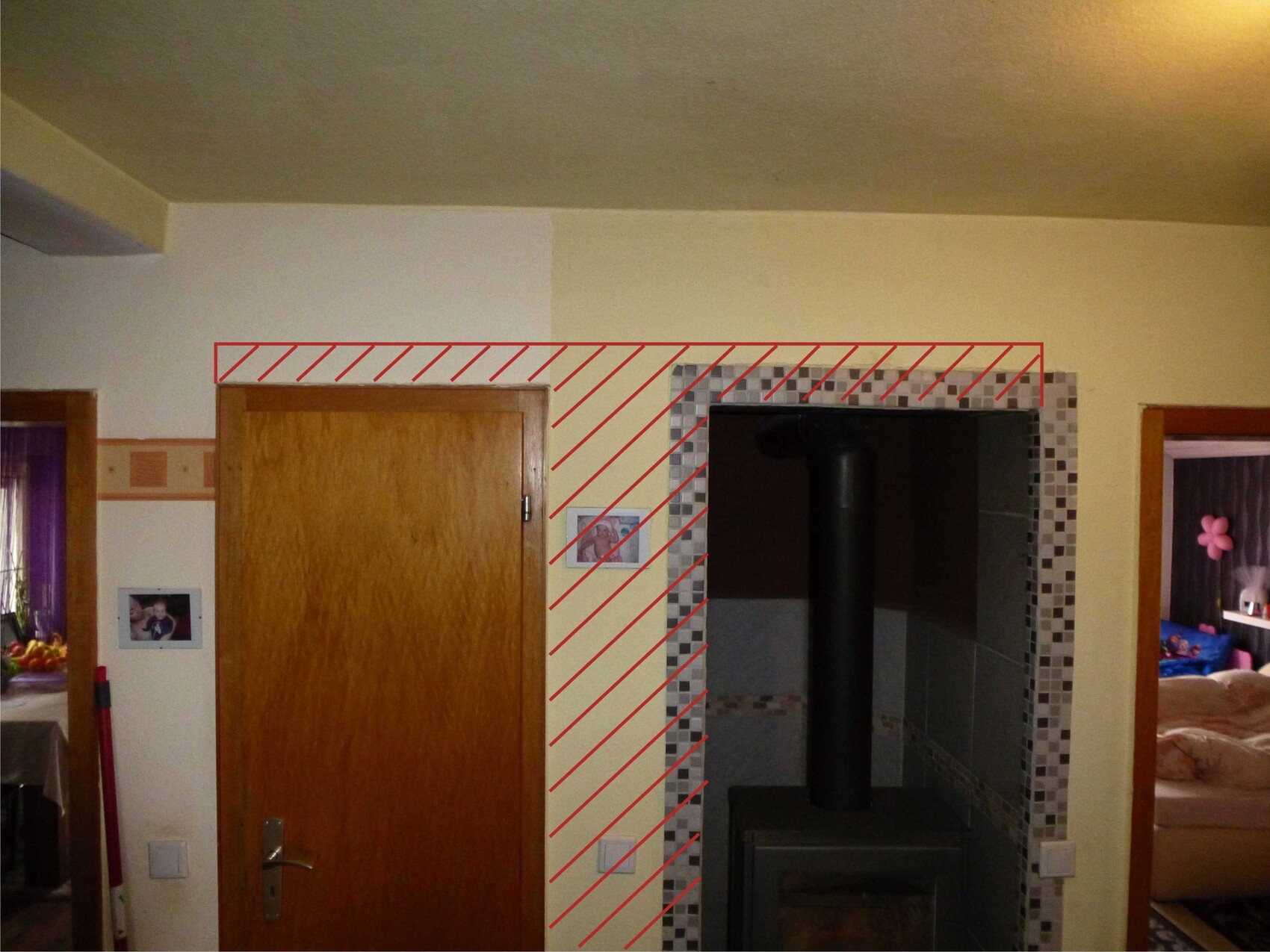 Living room with wood stove in a tiled niche, wooden door on the left, room visible on the right