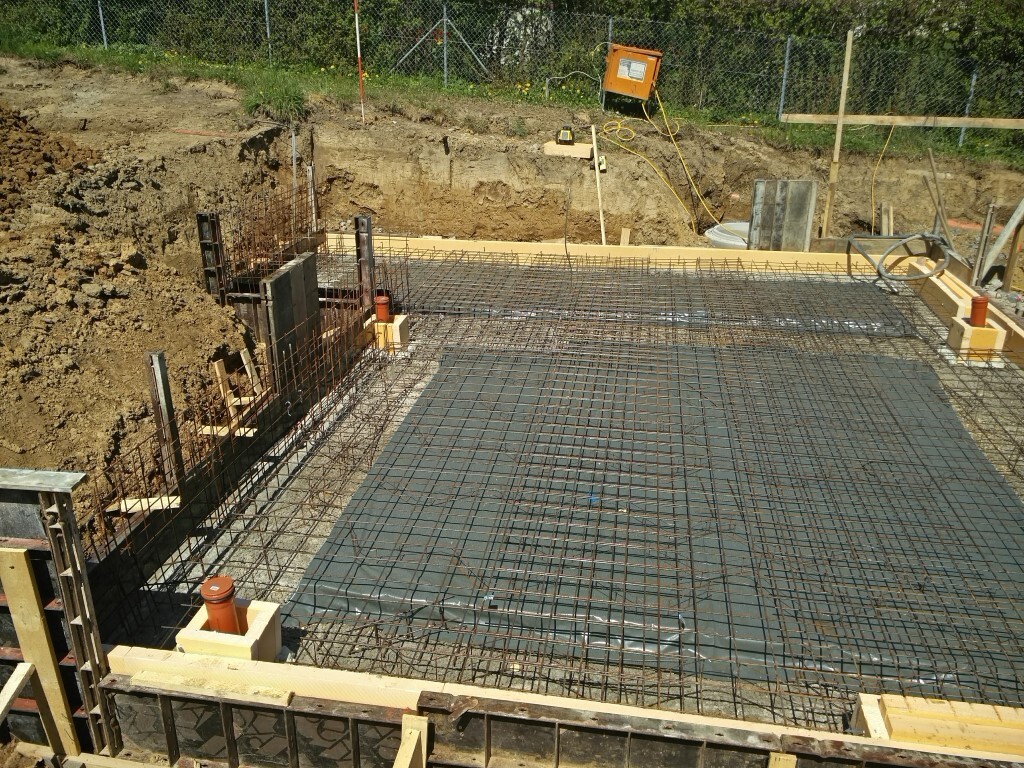 Foundation slab with reinforcing steel mesh, wooden formwork, and excavation pit.