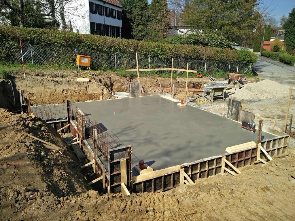 Freshly poured concrete slab on a construction excavation, wooden forms, and site tools visible.
