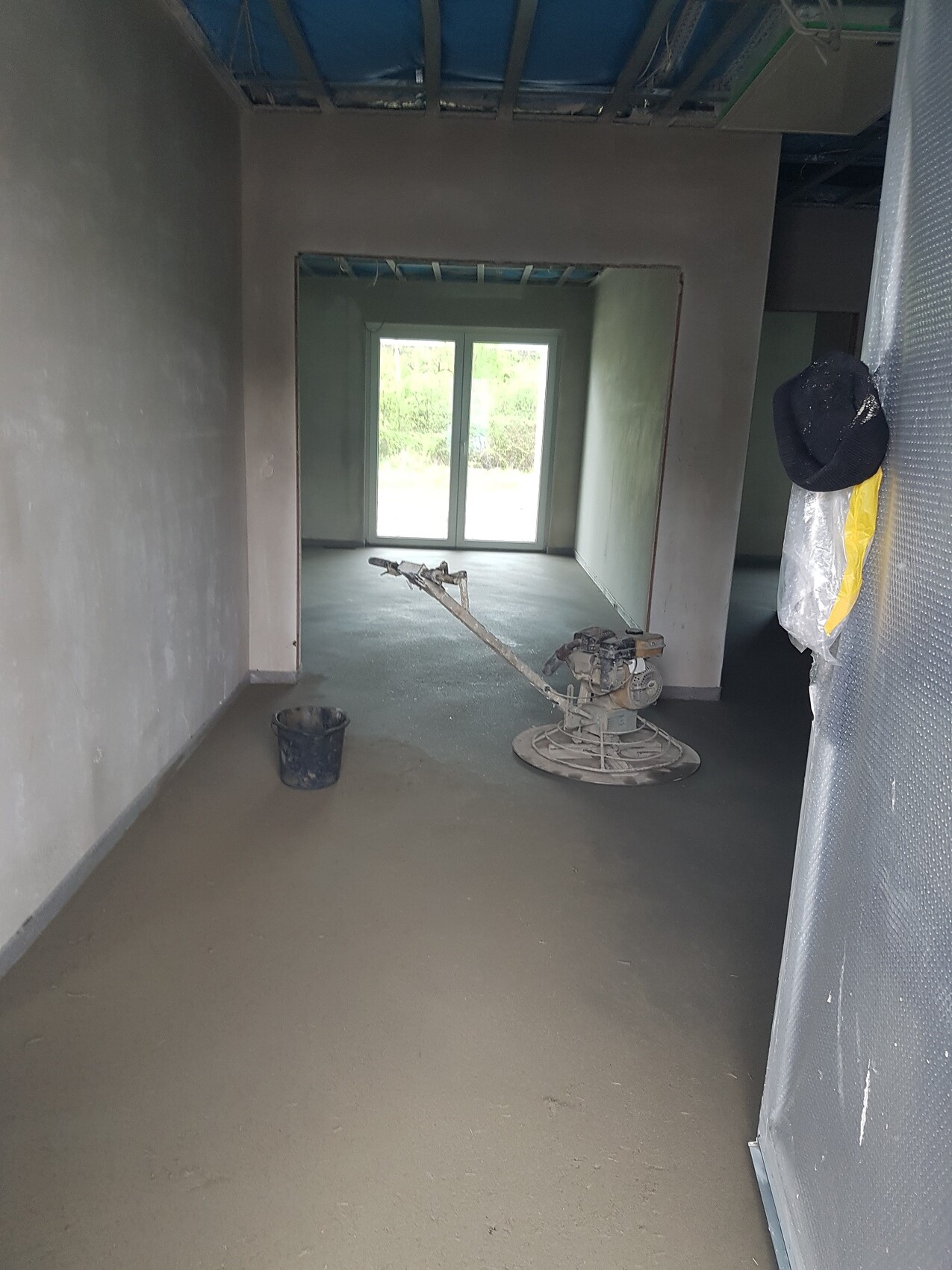 Interior construction site: unfinished interior, sanding machine, bucket, window front in the background