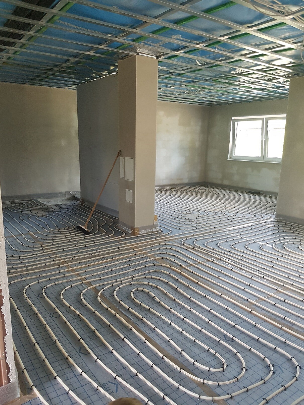 Underfloor heating pipes are being laid on insulation mats in an unfinished living space.
