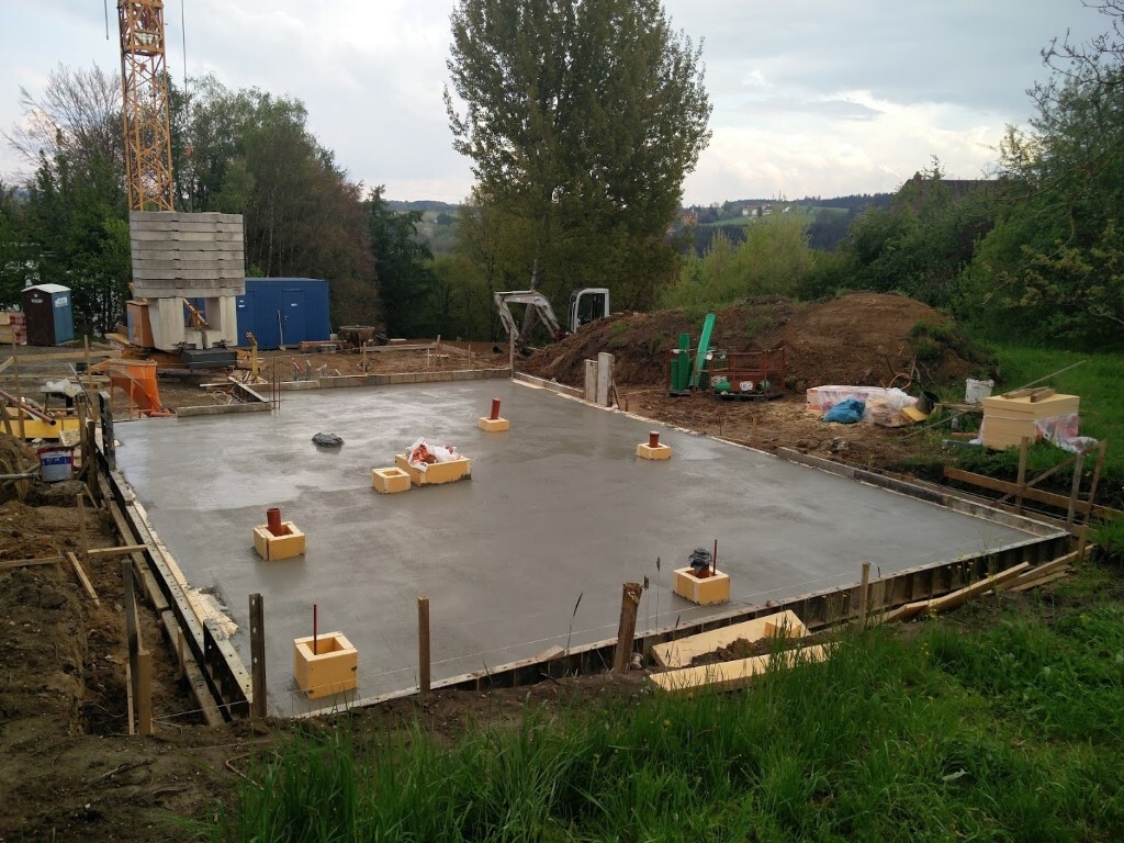 Concrete foundation slab at the construction site with anchors; crane on the left, materials in the background.