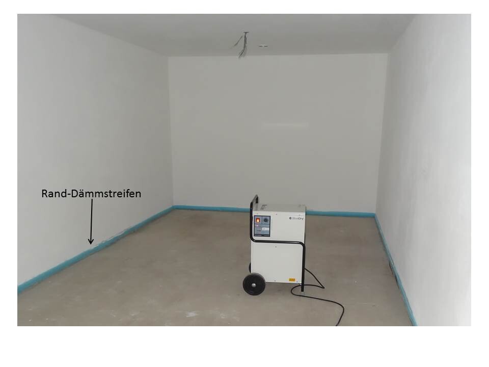 Empty interior space with edge insulation strips on the floor and a mobile construction device on wheels.