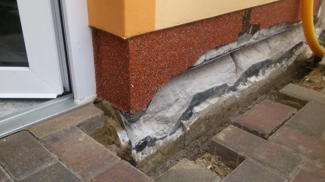 Exterior wall foundation with visible damage to plaster and foundation next to paving stones