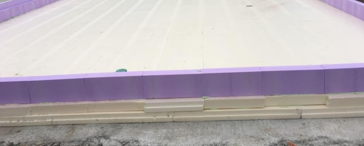 Violette Dämmplatten am Rand einer weißen Bodenplatte auf einer Baustelle; beige Streifen daneben.