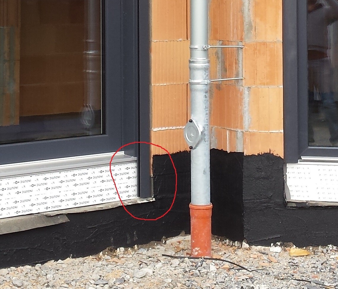 Exterior wall construction with window frame, gutter, and black sealing at the foundation