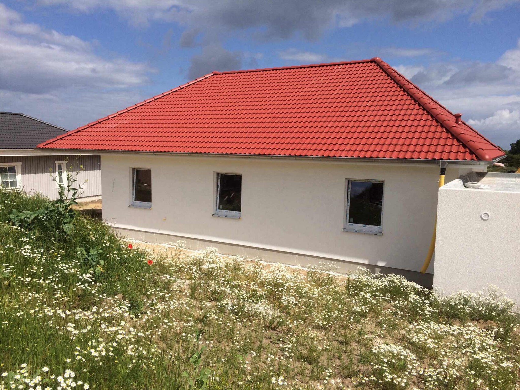 Single-family house with red tiled roof and white facade, three windows, wildflowers in the foreground.