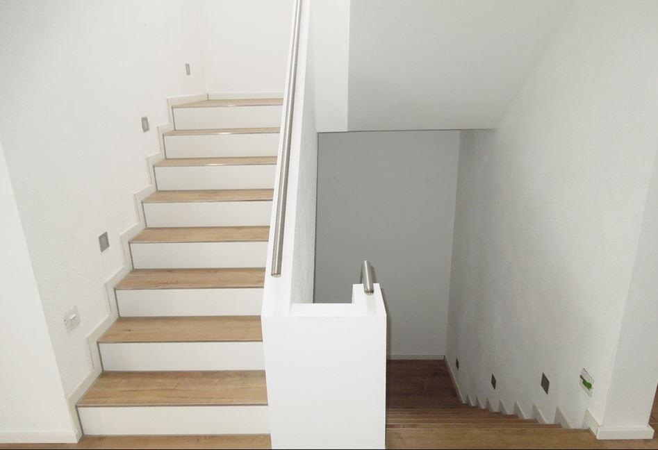 Modern interior staircase with wooden steps, white walls, and railing; view of two flights of stairs.