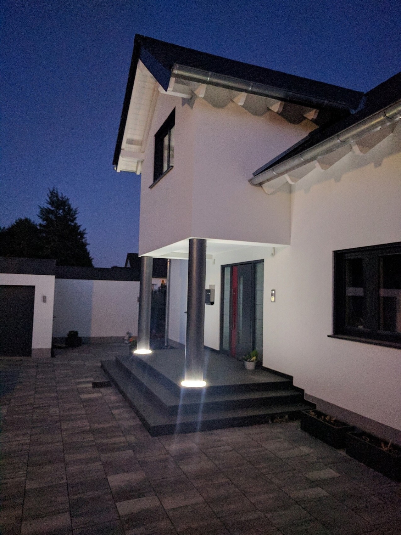 Moderne weiße Hausfassade mit beleuchteter Eingangstreppe und Säulen bei Nacht