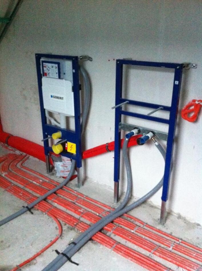 Two blue metal frames with sanitary and heating modules; red floor pipes and grey conduits.