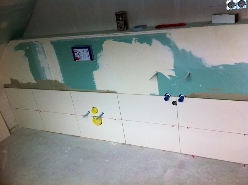 Bathroom renovation: tiling, visible pipes, green/blue painted wall surfaces.