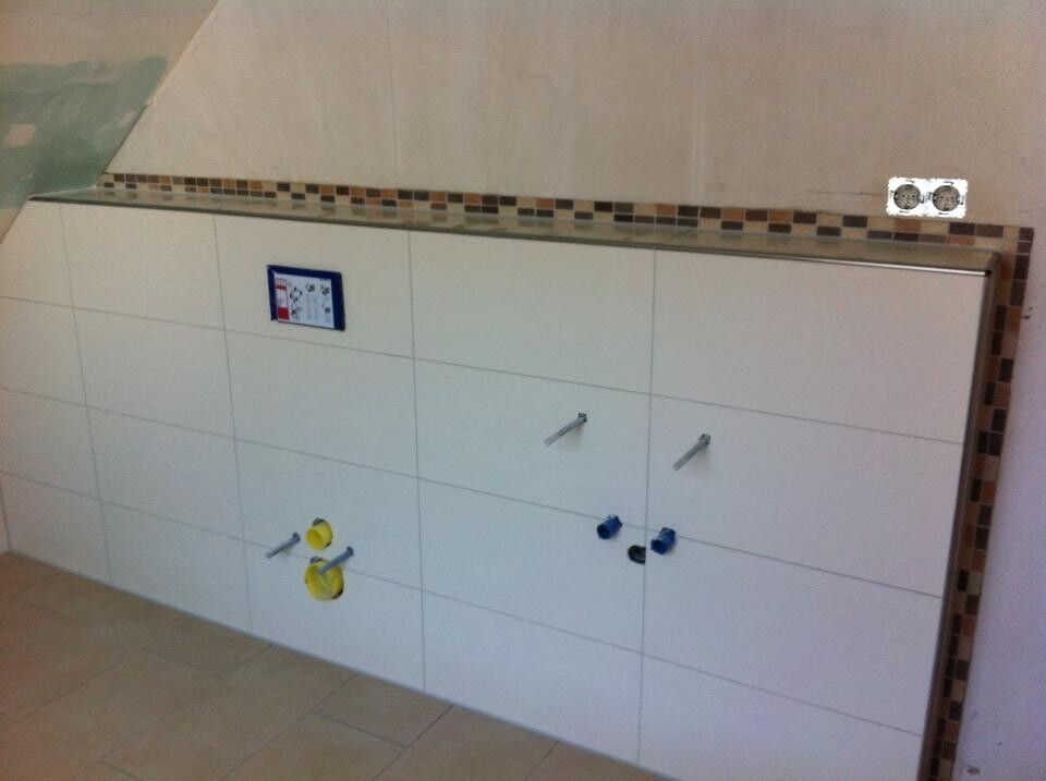 White bathroom vanity with two doors, visible water connections (yellow/blue) and tiled floor.