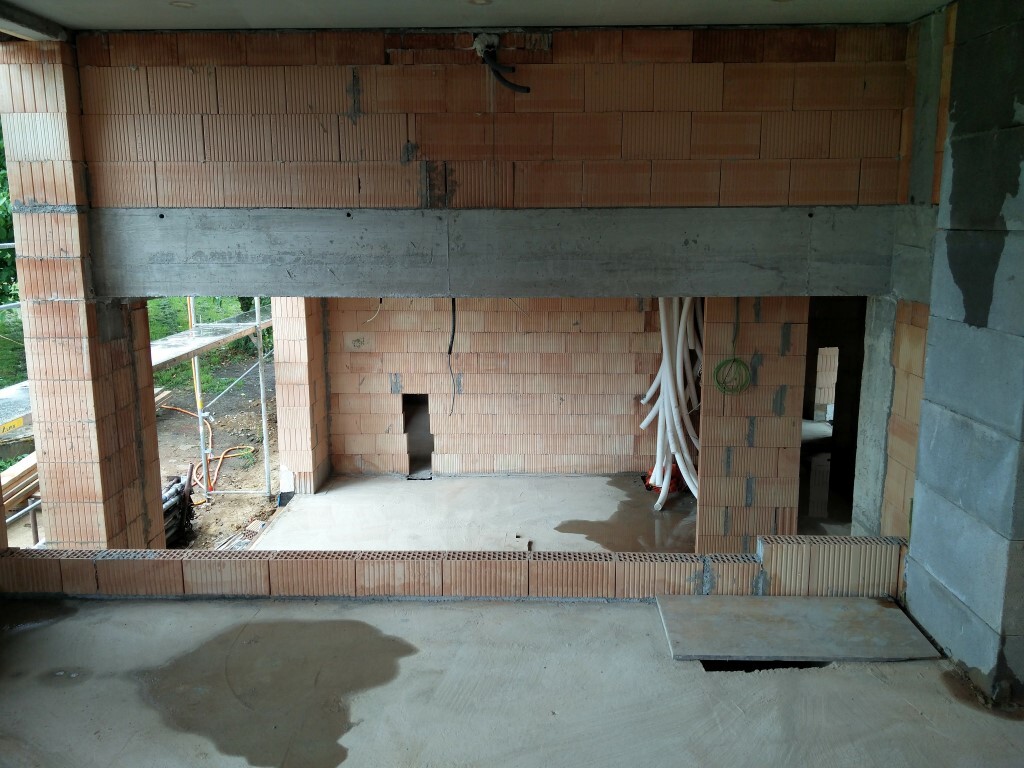 Baustelle im Innenraum: Ziegelwände, Betonbalken, Rohrleitungen und unfertiger Boden.