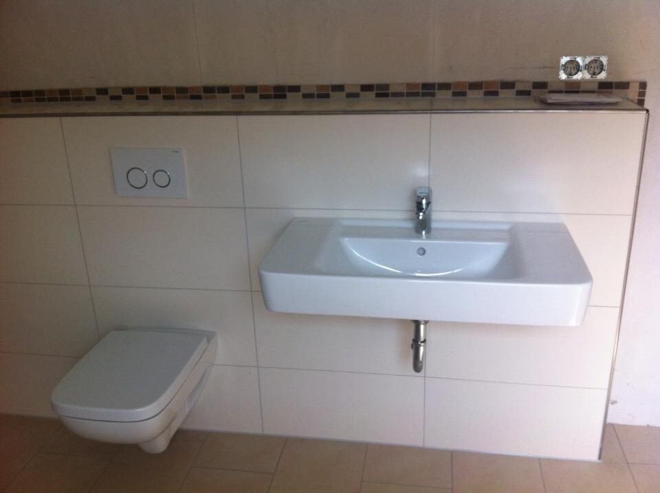 Modern bathroom: wall-mounted sink, wall-mounted toilet, and tiled border.