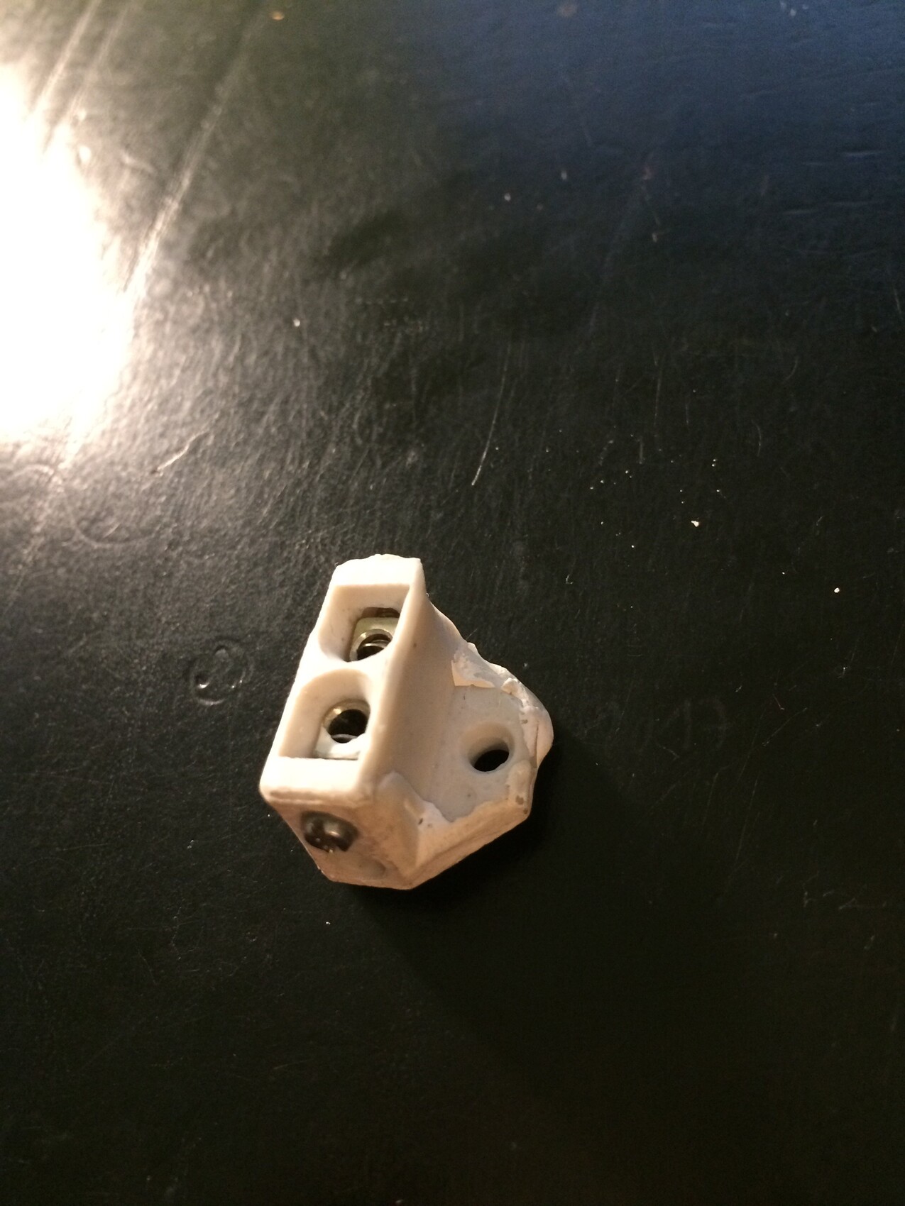 Small white terminal block made of plastic with screw terminals on a dark surface