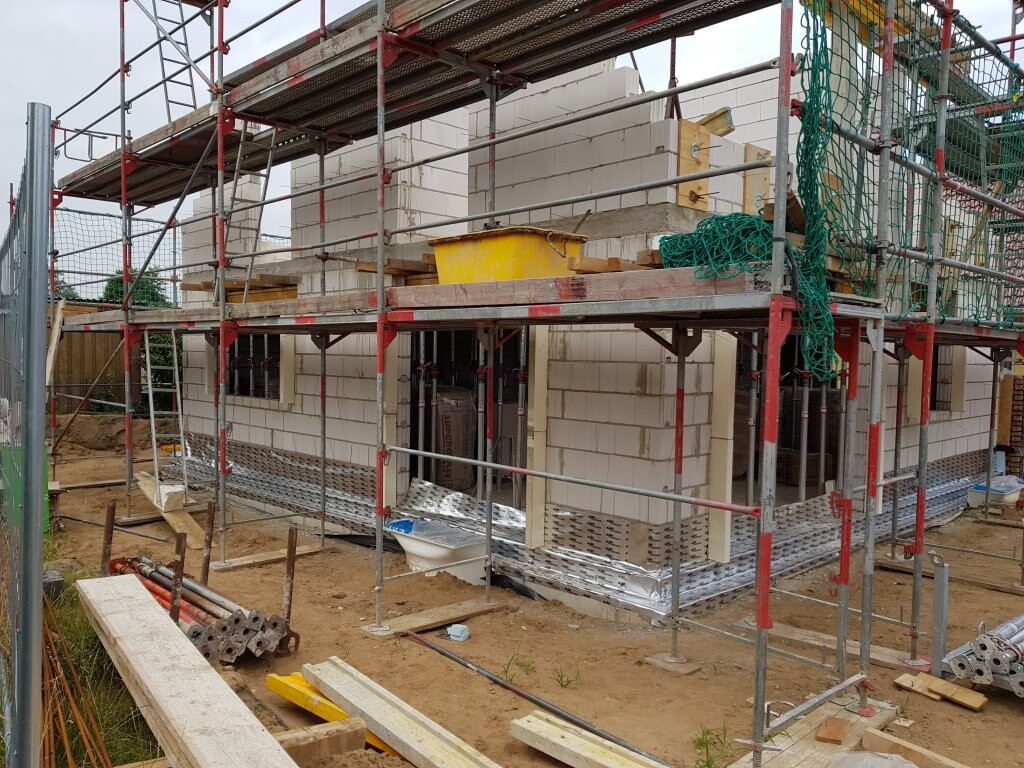 Construction site with scaffolding around masonry shell; building materials and tools ready.