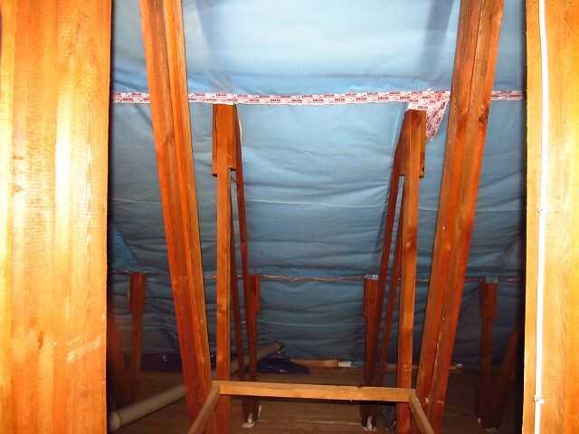 Attic with wooden rafters, blue insulation and beam structure, looking upwards.